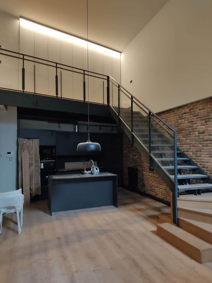 Escalera metálica y mezzanino en loft con pared de ladrillo visto por Kronos SL