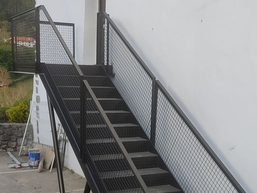 Escalera metálica exterior con barandilla de malla diamantada por Kronos SL, Bizkaia