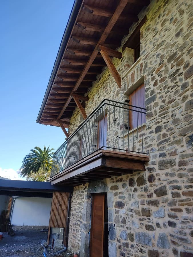 Barandilla metálica negra en balcón de casa de piedra fabricada por Kronos SL