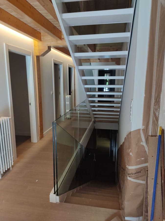 Escalera interior de acero con barandilla de cristal y vigas de madera por Kronos SL